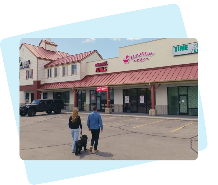 Two people walking a dog into the Scrubbin' Pup grooming store.